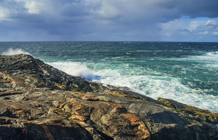 Rocky outcrop of ocean shore looking outwards towards the ocean, southern WA. Dark blue choppy water and breaking waves on rocks. Storm clouds out to sea.