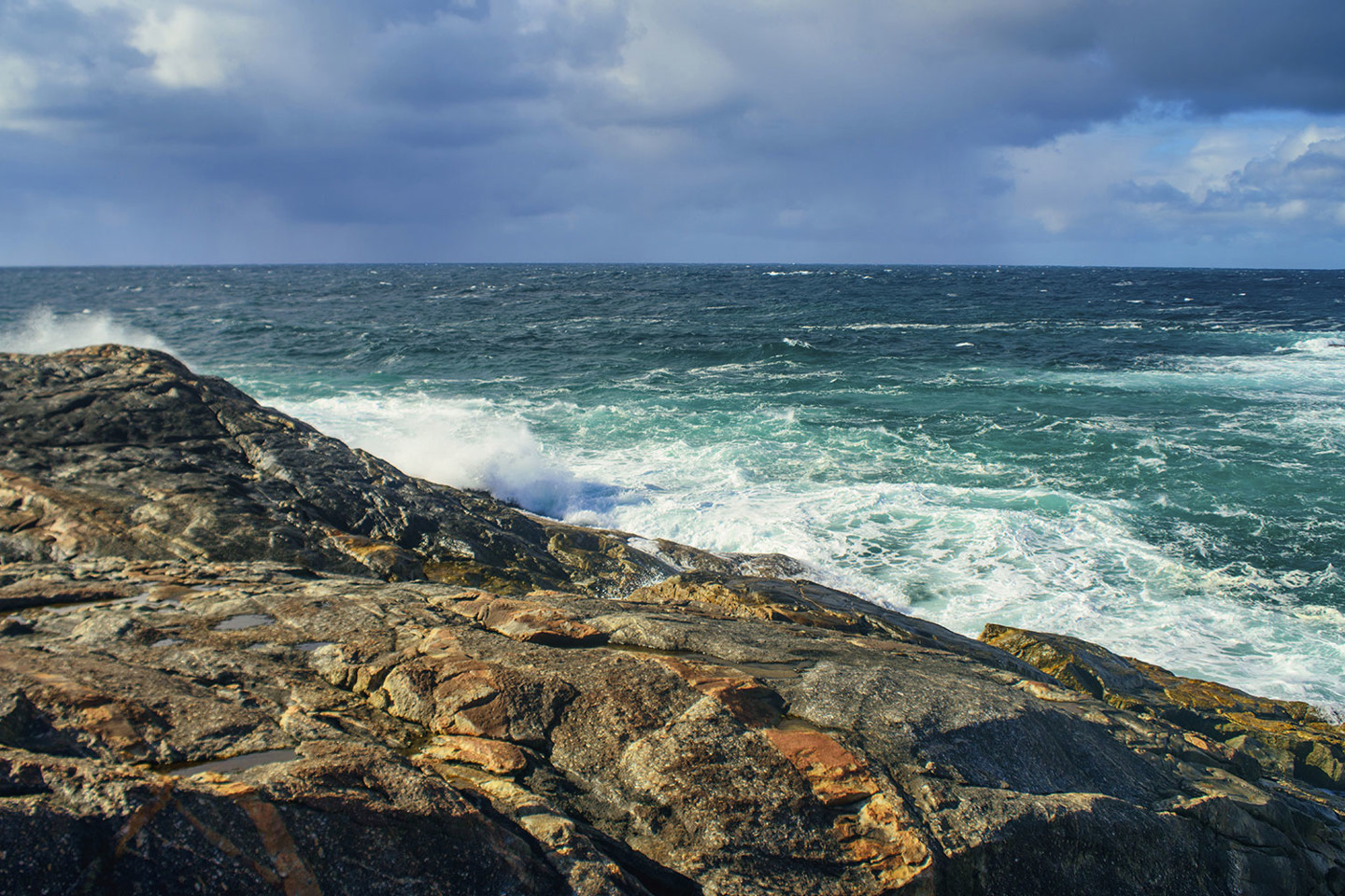 Rocky outcrop of ocean shore looking outwards towards the ocean, southern WA. Dark blue choppy water and breaking waves on rocks. Storm clouds out to sea.