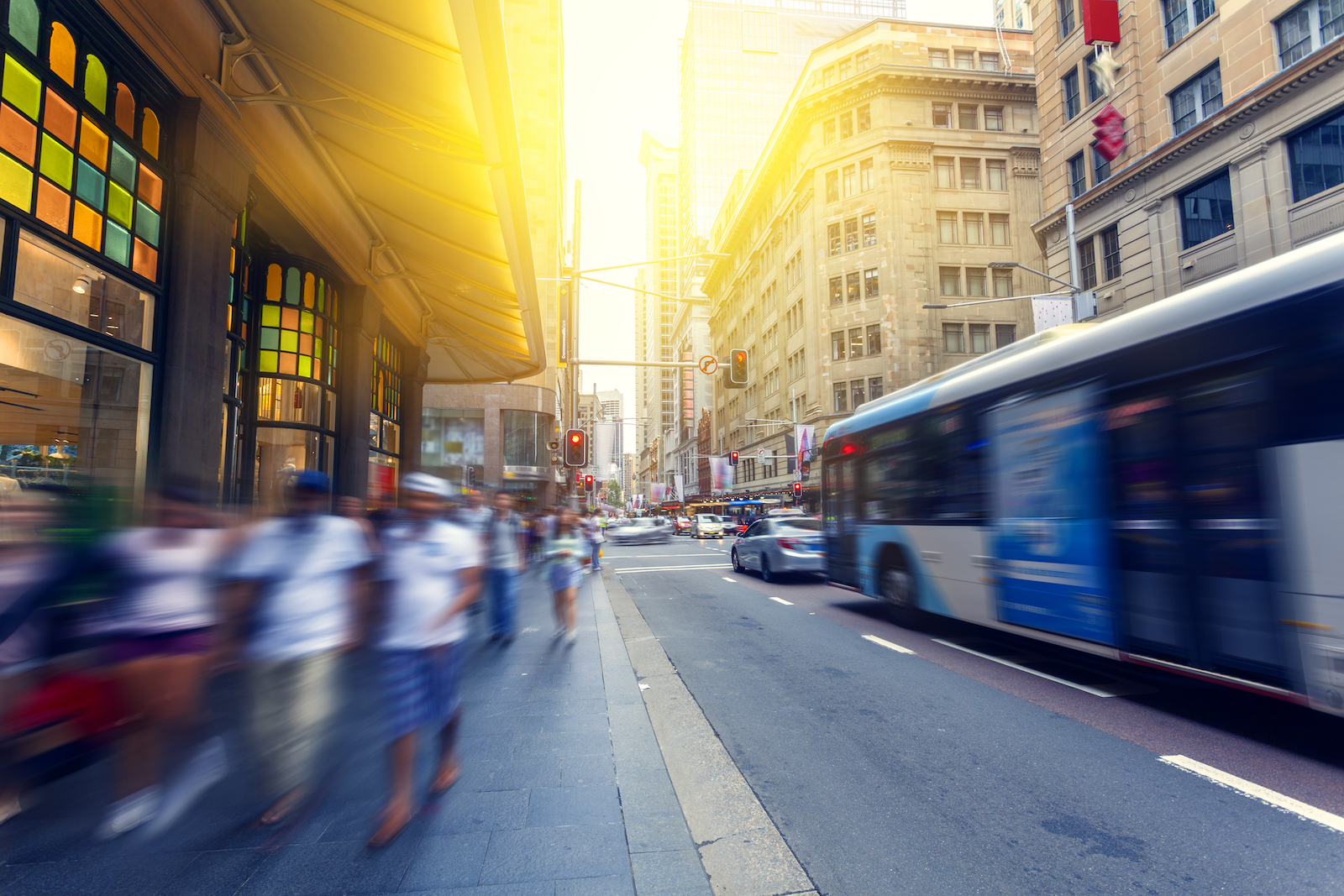 Pedestrians walking in the afternoon sun in Sydney CBD, NSW Australia. Buses, traffic and city buildings in the background.