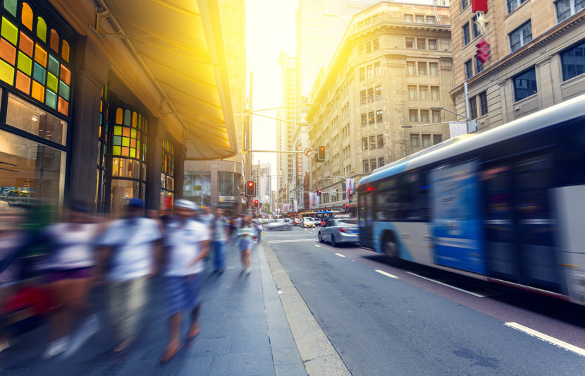 Pedestrians walking in the afternoon sun in Sydney CBD, NSW Australia. Buses, traffic and city buildings in the background.