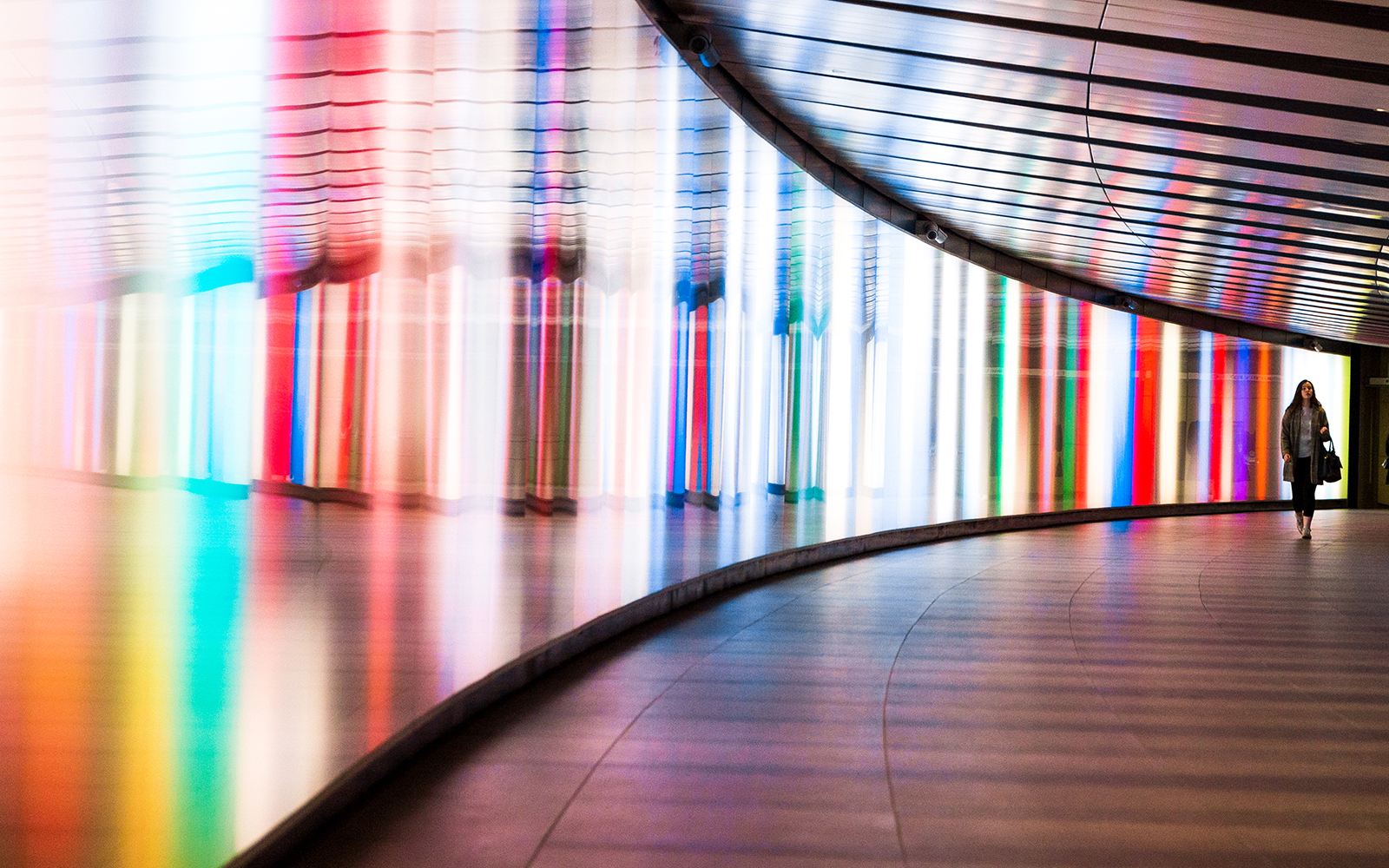 Woman walking past multiple coloured lights reflecting against a mirror