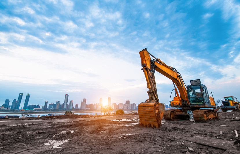 Excavators working on contaminated urban waterfront land with cityscape in background