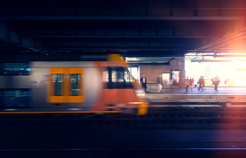 Train in Sydney moving past platform with pedestrians in the background.