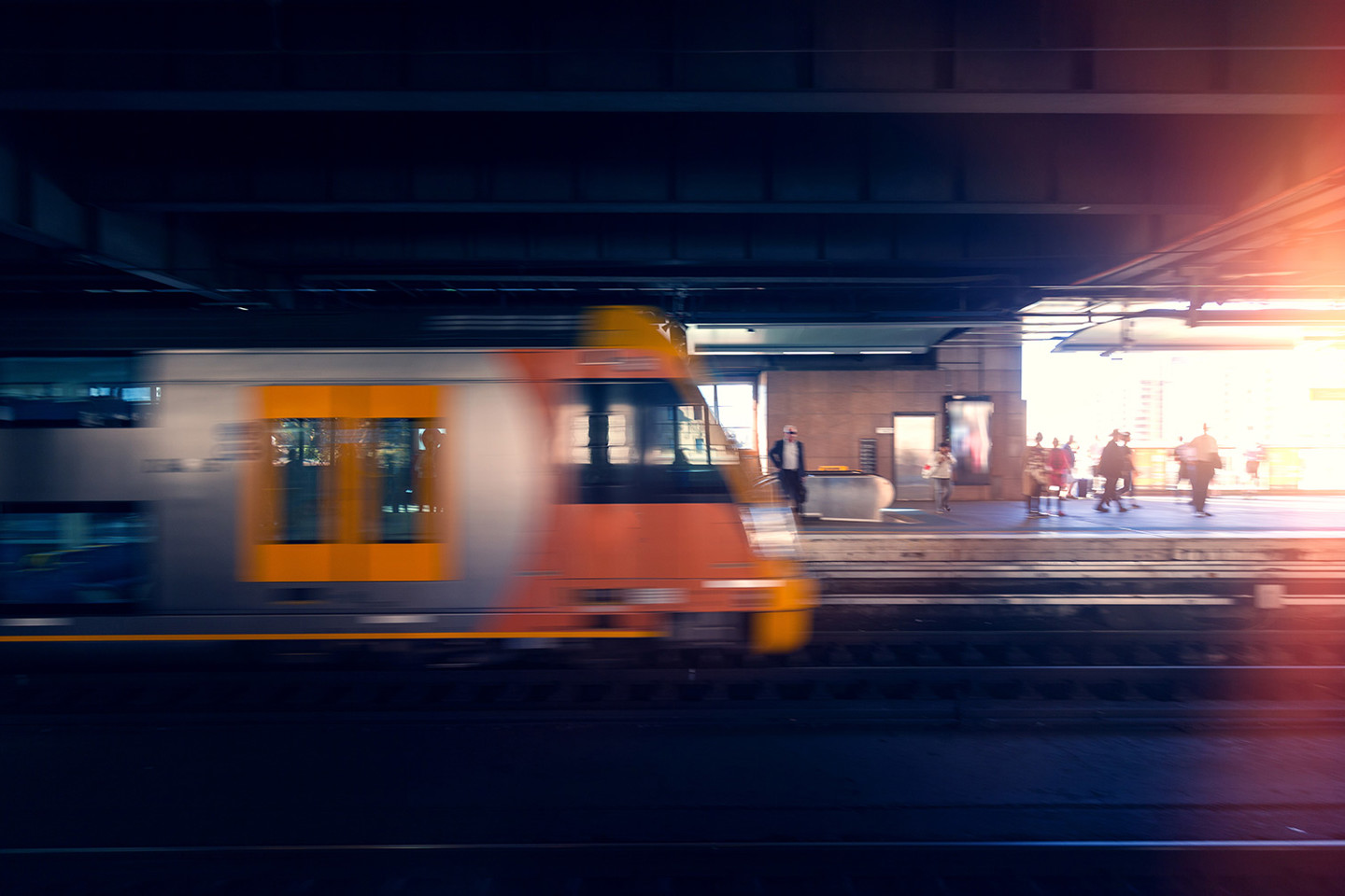 Train in Sydney moving past platform with pedestrians in the background.
