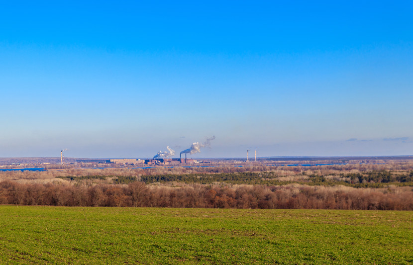green field and smoke pipes of factory at spring