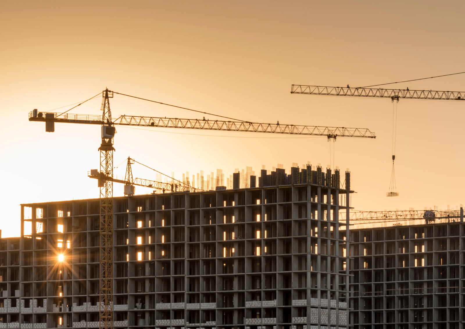 Building under construction at dusk. Orange sunset and cranes in the shadows 