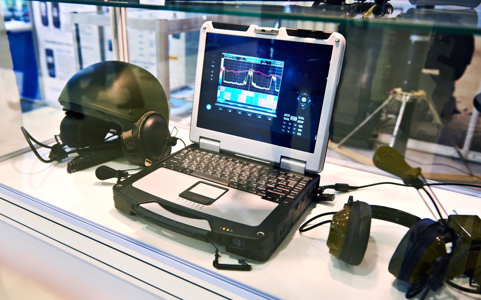 Defence equipment on shelf - computer with hard casing, tactical helmet and headphones.
