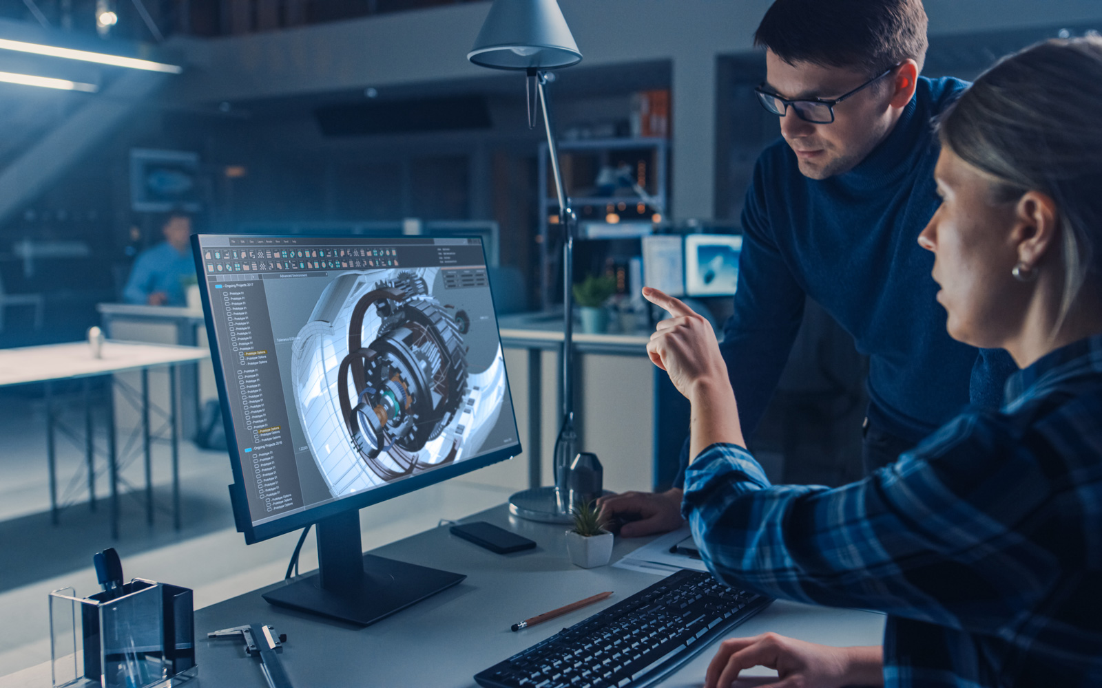 Systems engineer talking to designer over computer with CAD rendered turbine components on screen
