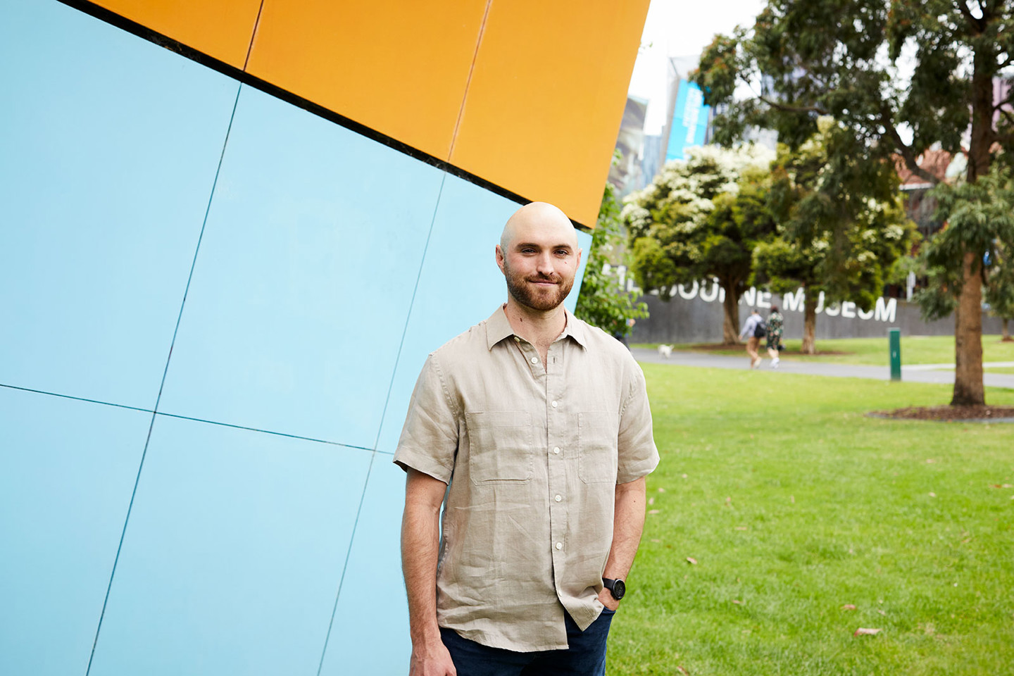 Stuart Scudamore, RPS Communications and engagement consultant stands outside of Melbourne Museum with orange and blue wall behind him.