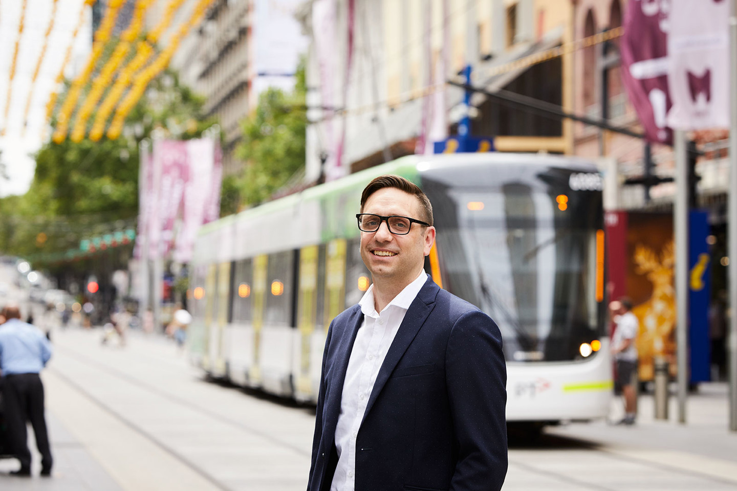 Paul Miziewiczs, RPS Principal Planner stands in busy Bourke Street Mall in Melbourne CBD with a tram behind him.