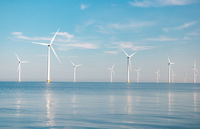 Offshore wind farm - white turbines in the mid-ground on calm blue waters, blue sky with clouds.