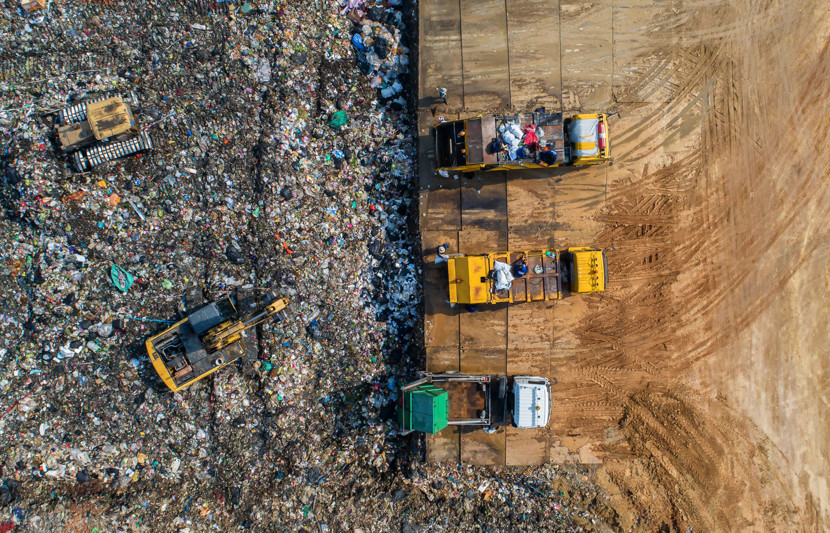 A birds eye view of landfill, with 5 trucks on the ground and thousands of plastic items