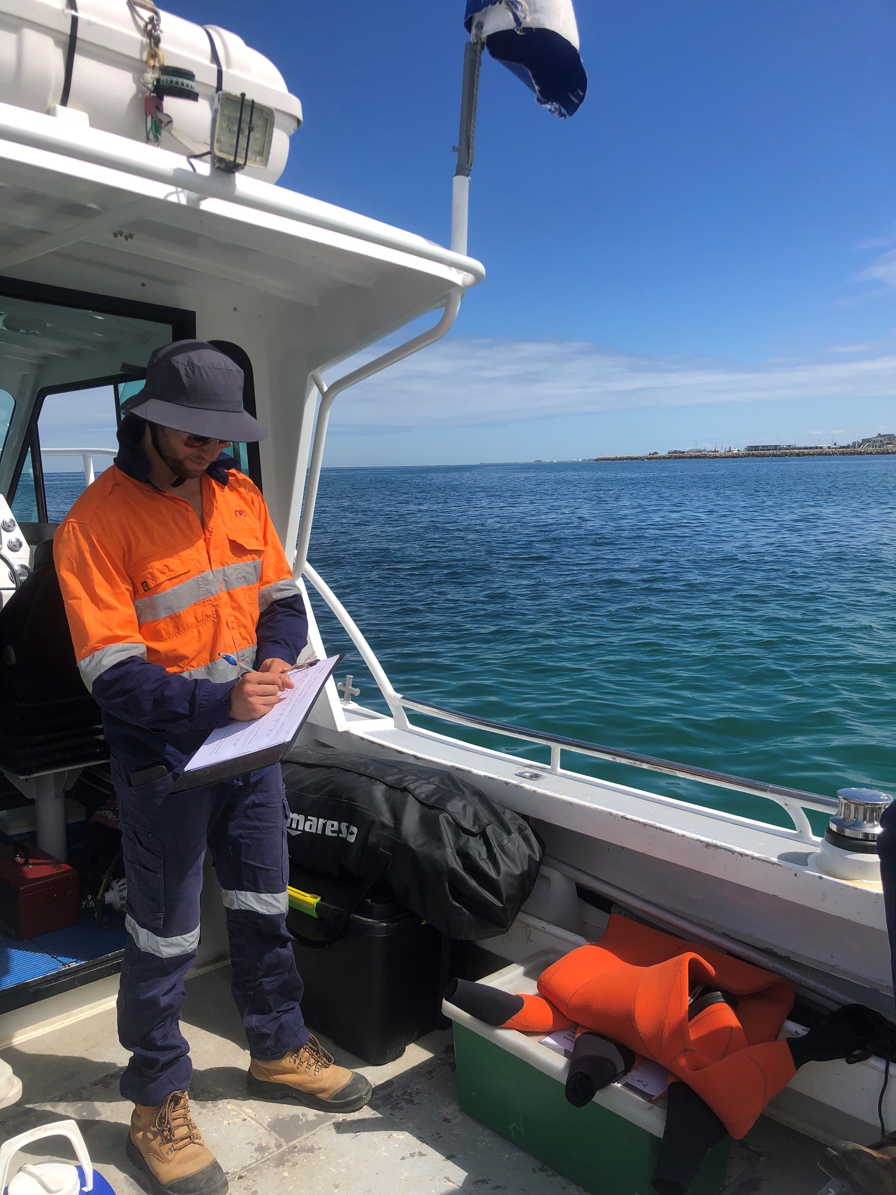 RPS marine scientist aboard a boat with clip board and hi-vis workwear while completing seagrass monitoring in the Cockburn Sound, between Perth and Rockingham in Western Australia.