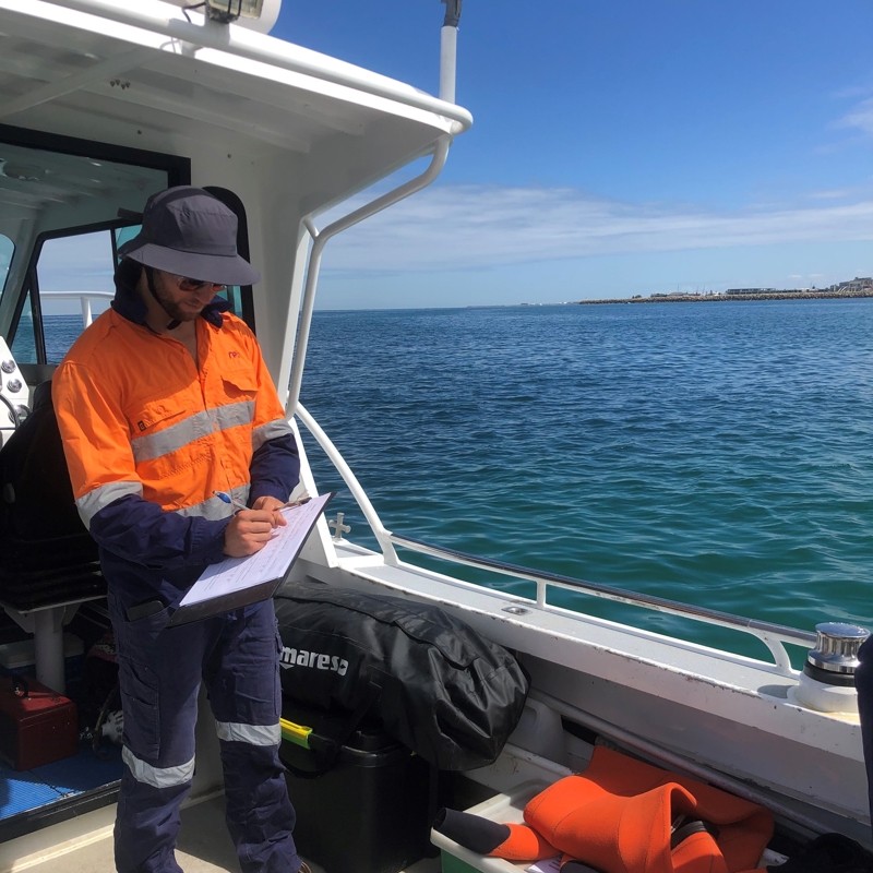 RPS marine scientist aboard a boat with clip board and hi-vis workwear while completing seagrass monitoring in the Cockburn Sound, between Perth and Rockingham in Western Australia.