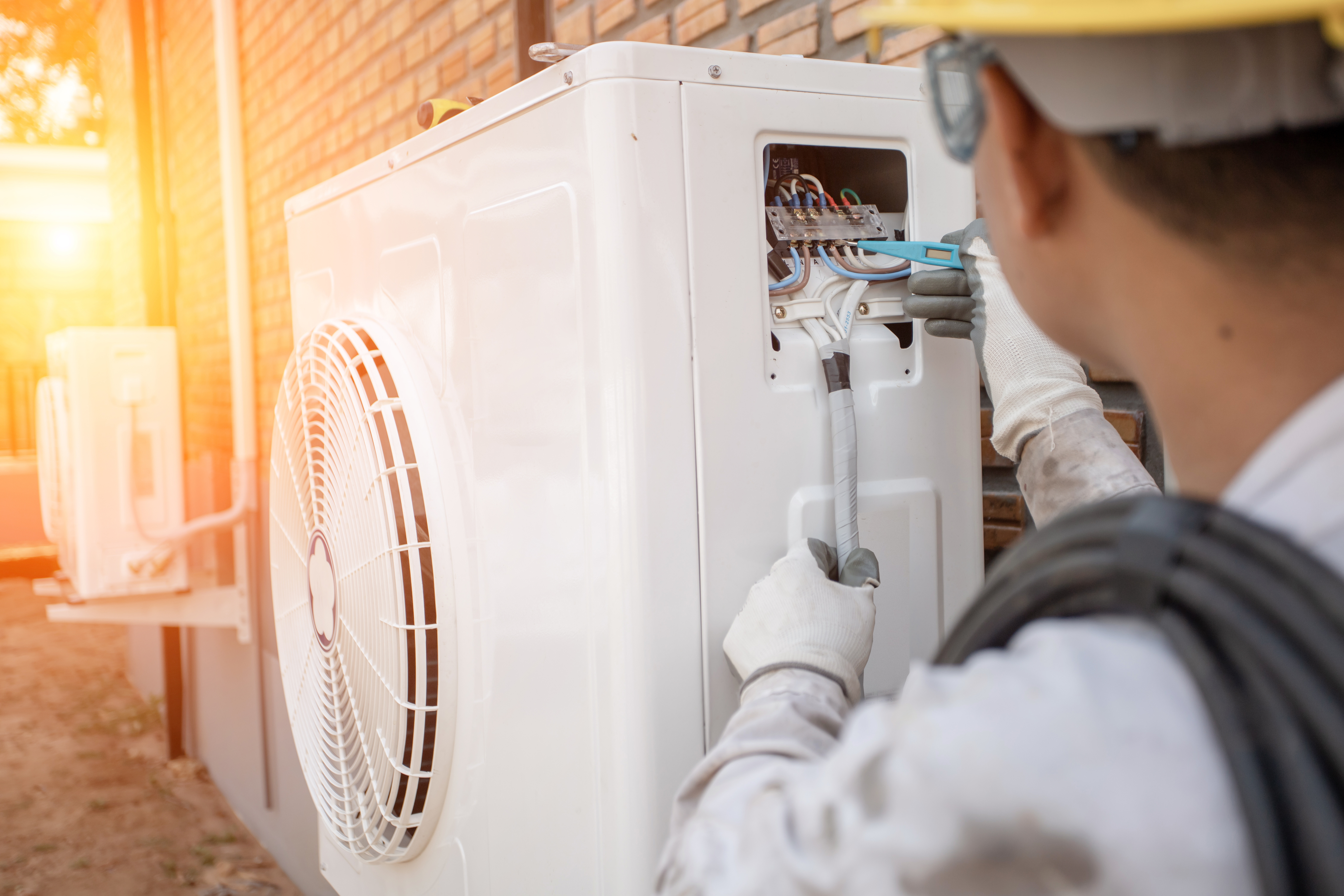 Man servicing heat pump unit on the side of wall