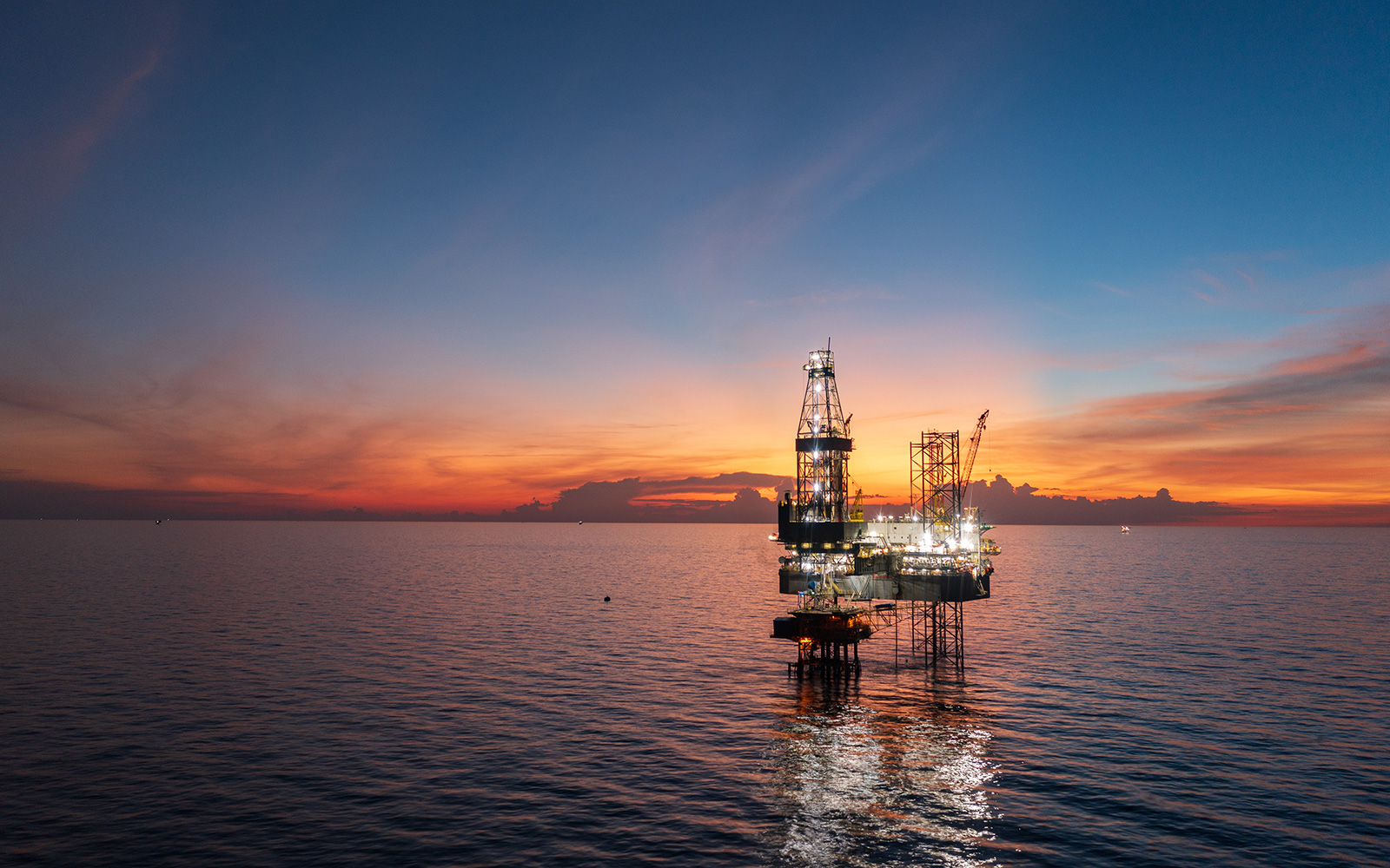 Offshore oil and gas platform at twilight. Lights reflecting in calm water